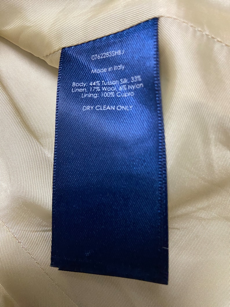 May include: A blue fabric label with white text that reads "07622835HB", "Made in Italy", "Body: 44% Tussan Silk, 33% Linen, 17% Wool, 6% Nylon", "Lining: 100% Cupro", and "DRY CLEAN ONLY".