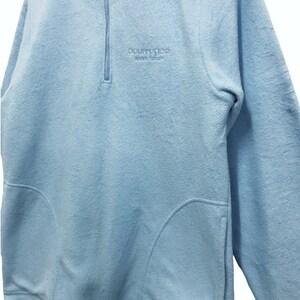 May include: A light blue fleece pullover with a half-zip closure and a small embroidered logo that reads "Country Classics Sport Leisure".