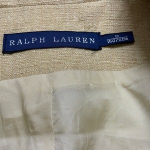 May include: A beige linen blazer with a blue label that reads "RALPH LAUREN" and "0 150/80A".