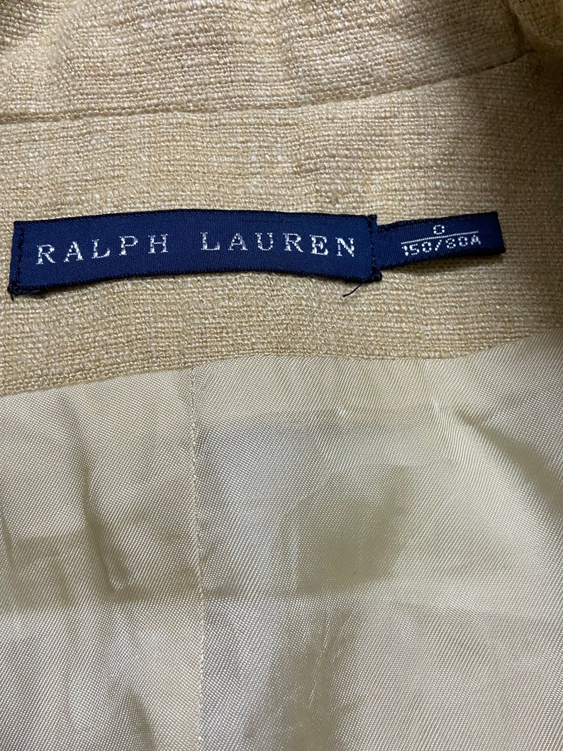 May include: A beige linen blazer with a blue label that reads "RALPH LAUREN" and "0 150/80A".