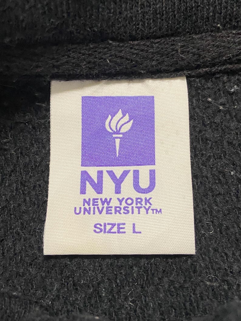 May include: A white tag with a purple logo of a torch and the text "NYU NEW YORK UNIVERSITY&trade; SIZE L"