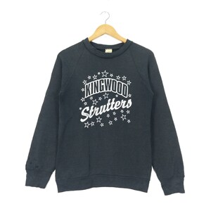 Könnte beinhalten: Ein dunkelgraues Sweatshirt mit einem weißen Grafikdruck von "KINGWOOD STRUTTERS" umgeben von weißen Sternen.