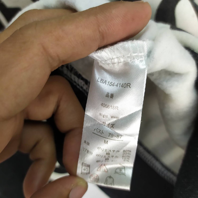 May include: A white tag with black text, LBA164-4140R, 品番 406618R, Night Wear, サイズ, バスト 79-87, M, 本体 ポリエステル 80%, リブ部分 ポリエステル 80%, ポリウレタン 20%,  40,  and a graphic of a triangle with a circle inside.