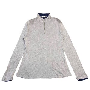 以下が含まれることがあります： 長袖のグレーのシャツで、4分の1ジッパー開閉です。 シャツはネイビーブルーの襟と袖口が付いています。 生地は柔らかいニット素材のようです。 シャツは白い表面に平らに置かれています。