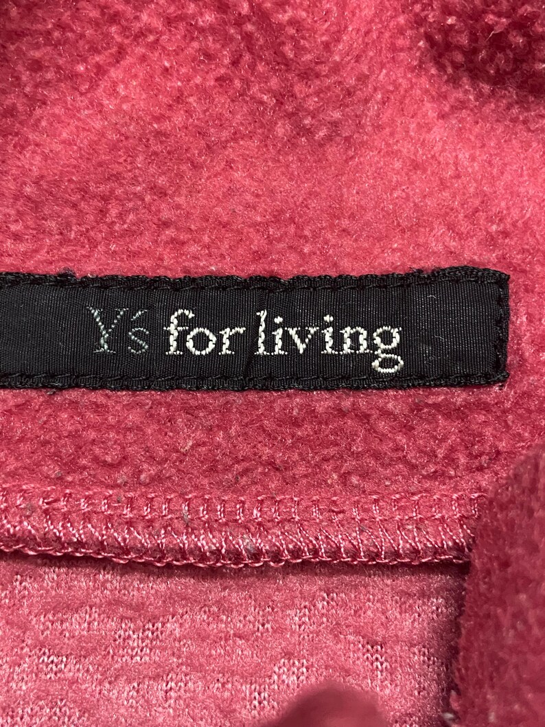 K&ouml;nnte beinhalten: Nahaufnahme eines roten Fleece-Stoffes mit einem schwarzen Etikett, auf dem "Y's for living" steht.