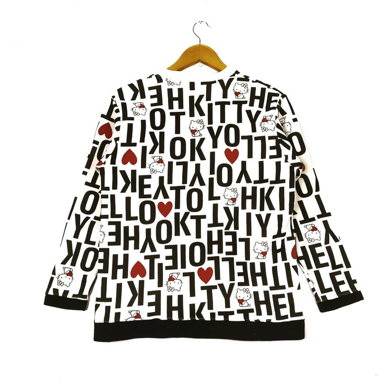 May include: White long-sleeved sweatshirt with a black and red print of Hello Kitty and the words "Hello Kitty" repeated in Korean and English.