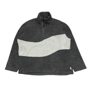 Op de afbeelding: Een grijze fleece trui met een wit golfontwerp en een rits. De trui heeft een klein zwart label met witte tekst.