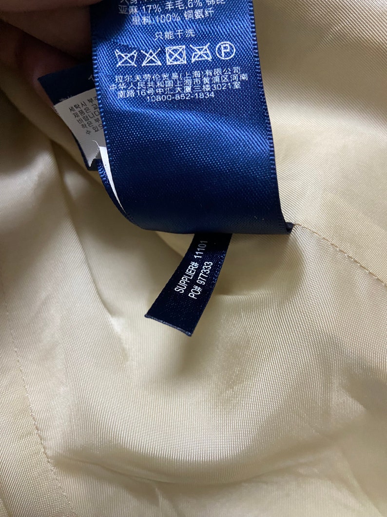 May include: A blue fabric label with white text and symbols. The text includes "17% Wool, 6% Linen, 100% Cotton", "Dry Clean Only", "Supplier# 11101", and "PO# 977333".