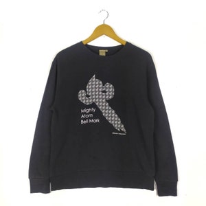 May include: Black long-sleeve sweatshirt with a graphic print of a stylized figure and the text "Mighty Atom Bell Mark".