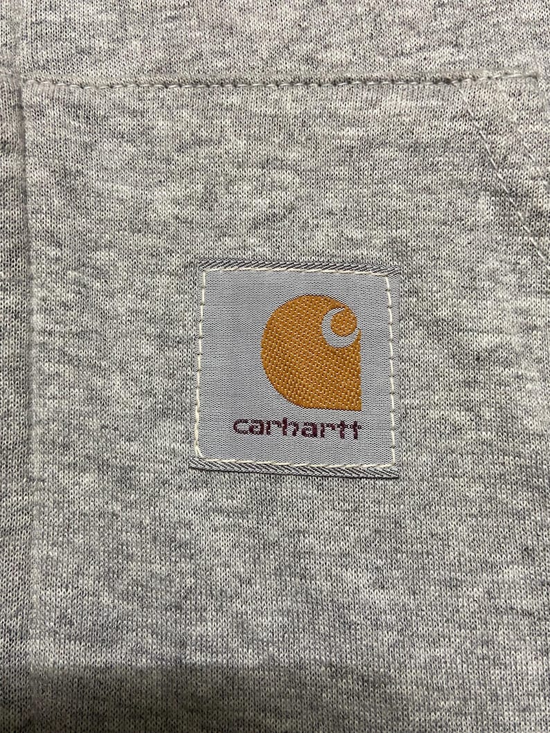 May include: A gray Carhartt workwear patch with a brown logo and the word "carhartt" in white lettering.