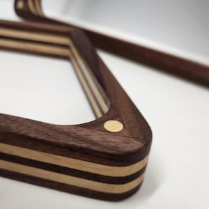 May include: A wooden pool rack with a dark brown walnut finish and light wood accents. The rack has a triangular shape and is made of multiple layers of wood. The rack has a small, round, light wood accent on each corner.