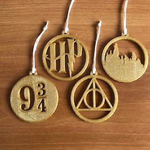 Può includere: Quattro ornamenti rotondi dorati ricoperti di glitter con diversi design a tema Harry Potter. Gli ornamenti presentano lo stemma di Hogwarts, il simbolo dei Doni della Morte, il numero di banchina dell'Espresso di Hogwarts "9 3/4" e una silhouette del castello di Hogwarts.