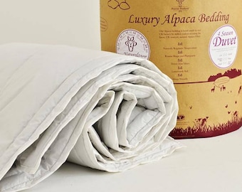 May include: A white alpaca duvet rolled up, with a brown box in the background. The box has the text "Luxury Alpaca Bedding" and "4 Season Duvet" printed on it.