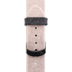 Può includere: Un cinturino da orologio in feltro rosa chiaro con una fibbia nera e un accento in feltro grigio. Il cinturino è realizzato da "The Strap Loops".