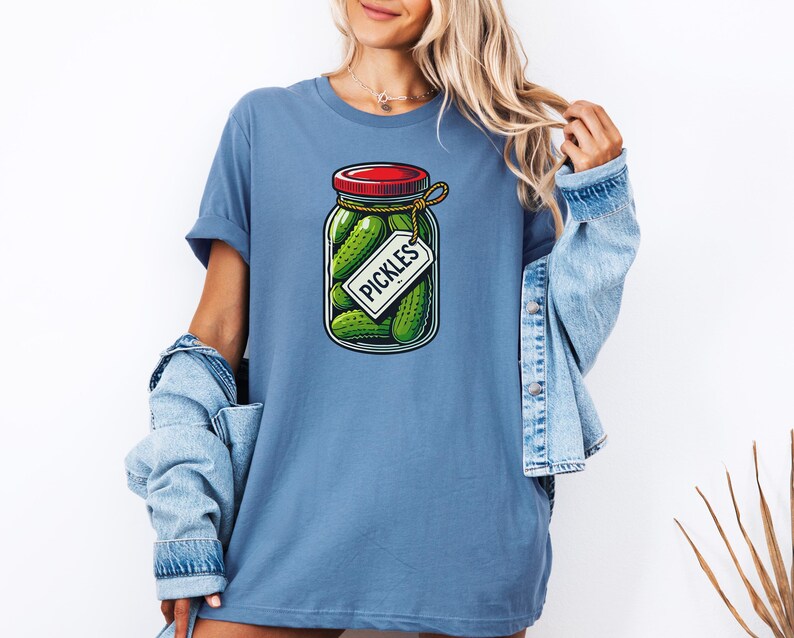 K&ouml;nnte beinhalten: Ein blaues T-Shirt mit einem Aufdruck eines Glases mit Gurken. Das Glas hat einen roten Deckel und ein Etikett mit der Aufschrift "PICKLES".