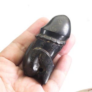 Può includere: Una scultura in legno intagliato marrone scuro con intricati motivi floreali. La scultura ha una parte superiore arrotondata e una base strutturata. L'oggetto è tenuto in mano su sfondo bianco.