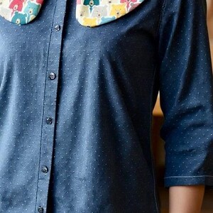 May include: A blue shirt with a white polka dot pattern and a large, rounded collar. The collar is decorated with a colourful bear print. The sleeves are three-quarter length.
