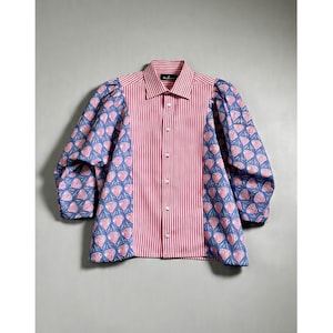 May include: A button-down shirt with a red and white striped body and blue patterned sleeves. The sleeves feature a repeating design of pink heart-shaped motifs. The shirt has a classic collar and long sleeves.