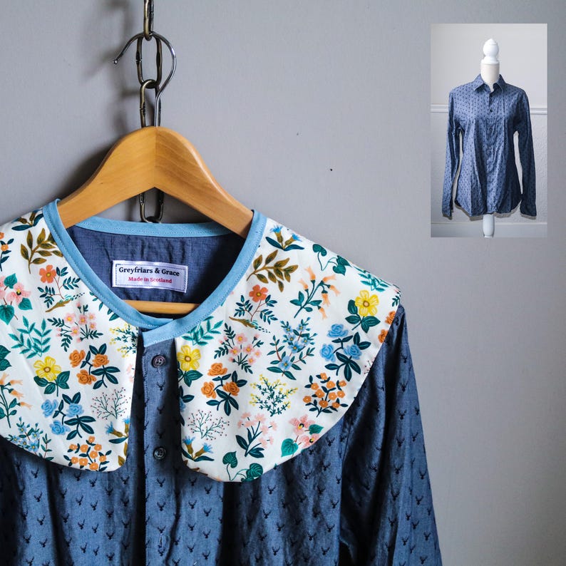 May include: A blue button-down shirt with a detachable floral collar. The collar features a white background with a colorful floral pattern. The shirt is hanging on a wooden hanger against a gray background. The label reads "Greyfriars & Grace Made in Scotland."