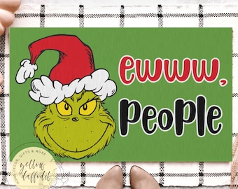 Puede incluir: Felpudo verde con la cara del Grinch con gorro de Papá Noel. El texto "ewww. People" está en rojo y negro. La alfombra rectangular está sobre una superficie a cuadros blancos y negros.