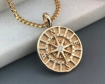 May include: A gold compass necklace with a small diamond in the center. The compass is surrounded by a textured circle with the letters N, E, S, and W.