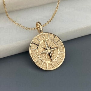 May include: Gold compass necklace with a detailed compass design and a chain. The compass features a star in the center and the cardinal directions are marked around the edge.