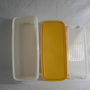 May include: Three rectangular plastic containers, one white, one yellow, and one clear with a grid pattern. The containers are for storing food.