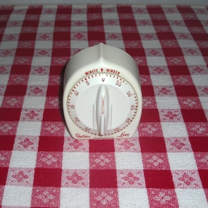 May include: A cream-colored Lux Minute Minder kitchen timer with a central rotating dial. The face features red numerical markings from 0 to 55, with the text "MINUTE MINDER" printed at the top and "Robertshaw Lux" at the bottom in red lettering.