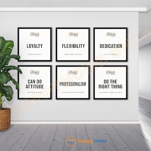May include: Six framed motivational posters with black frames and white backgrounds. The posters display words like "Loyalty," "Flexibility," and "Dedication," along with related phrases. A potted plant sits to the left of the posters.