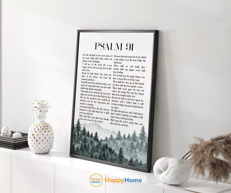 May include: A framed print featuring Psalm 91 text with a forest scene at the bottom. The black frame surrounds the white text and a grayscale image of trees. The print is displayed on a white surface.