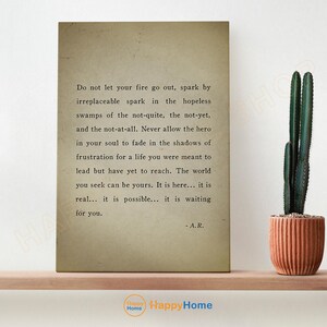 Op de afbeelding: Een ingelijste print met inspirerende tekst op een vintage achtergrond. De tekst luidt: "Laat je vuur niet doven..." en is gesigneerd "- A.R." Een cactus in een terracotta pot staat rechts.