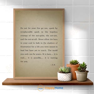 Op de afbeelding: Een ingelijste print met een citaat op een neutrale achtergrond, weergegeven op een houten plank. Het citaat luidt: "Laat je vuur niet uitgaan..." en is gesigneerd "- A.R." Verschillende vetplanten in potten staan op de plank.