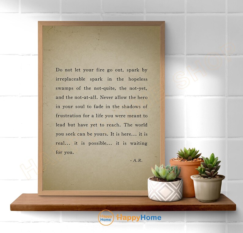 Op de afbeelding: Een ingelijste print met een citaat op een neutrale achtergrond, weergegeven op een houten plank. Het citaat luidt: "Laat je vuur niet uitgaan..." en is gesigneerd "- A.R." Verschillende vetplanten in potten staan op de plank.