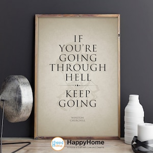 May include: A framed print with the quote "IF YOU'RE GOING THROUGH HELL KEEP GOING" by Winston Churchill. The print has a light beige background and a wooden frame. Decorative items, including white vases and a candle holder, are on a wooden surface.