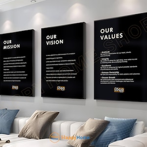 May include: Three framed black wall art pieces with white text. The first reads "OUR MISSION", the second "OUR VISION", and the third "OUR VALUES". Below each text is a logo. The art hangs above a white sofa with blue and grey cushions.