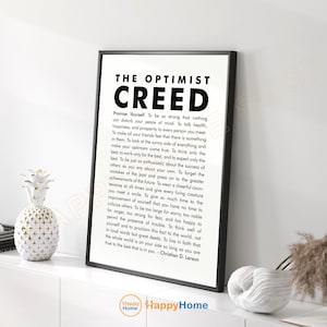 Op de afbeelding: Een zwart-wit ingelijste print met de tekst "THE OPTIMIST CREED" en een lange inspirerende quote. De print wordt weergegeven op een wit oppervlak met decoratieve items, waaronder een ananasvormige vaas.