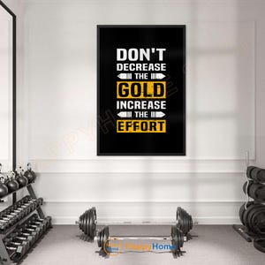 May include: A framed motivational poster with the text "DON'T DECREASE THE GOLD INCREASE THE EFFORT" in white and gold against a black background. The image is in a gym setting with weights and exercise equipment.