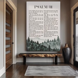 May include: A framed canvas print featuring the text of Psalm 91 in black font. Below the text is a watercolor landscape of a forest and mountains. The print hangs above a wooden bench.