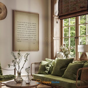 Op de afbeelding: Een ingelijste print met een citaat in een woonkamer. De print heeft een beige achtergrond met zwarte tekst. De kamer heeft een groene bank met kussens, een houten salontafel en een raam met natuurlijk licht.