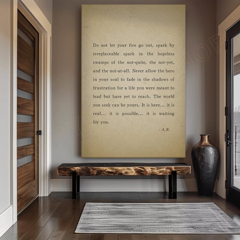 Op de afbeelding: Een ingelijste print met inspirerende tekst in een neutraal kleurenpalet hangt boven een houten bank. De tekst luidt: "Do not let your fire go out..." en is gesigneerd "-A.R." Een decoratieve vaas staat in de buurt.