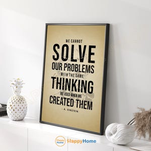 May include: A framed print with a black frame and a tan background. The print features the quote "WE CANNOT SOLVE OUR PROBLEMS WITH THE SAME THINKING WE USED WHEN WE CREATED THEM" by A. Einstein in bold black text. Decorative items are on the white shelf.