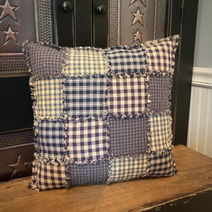 May include: A blue and white patchwork pillow with frayed edges. The pillow is made of different plaid and gingham fabrics.