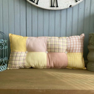 May include: A yellow, pink, and brown patchwork lumbar pillow with three white buttons. The pillow is made of different plaid and gingham fabrics.