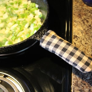May include: A black cast iron skillet with a checkered fabric handle, filled with sauteed onions and green peppers.