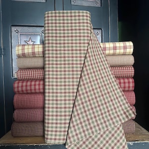 May include: A stack of fabric rolls in various plaid patterns. The dominant roll features a green, red, and cream plaid, with other rolls in shades of red, cream, and brown. The fabric is likely cotton or a similar material, suitable for quilting or crafting projects.