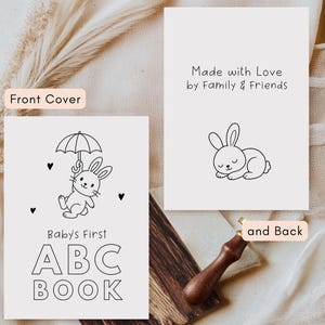May include: Black and white illustration of a baby's first ABC book with a bunny holding an umbrella. The cover text reads "Baby's First ABC BOOK". The back of the book has a sleeping bunny and the text "Made with Love by Family & Friends".