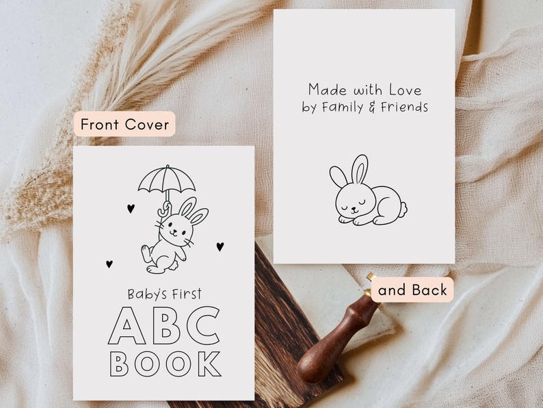 May include: Black and white illustration of a baby's first ABC book with a bunny holding an umbrella. The cover text reads "Baby's First ABC BOOK". The back of the book has a sleeping bunny and the text "Made with Love by Family & Friends".