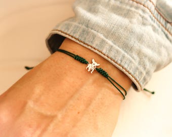 May include: A green string bracelet with a silver chihuahua charm.