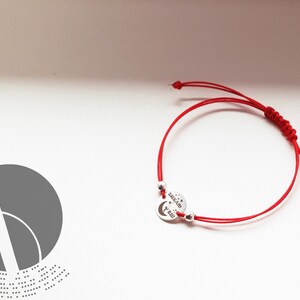 Op de afbeelding: Rood koord armband met een zilveren bedel met de tekst "Dream Big".