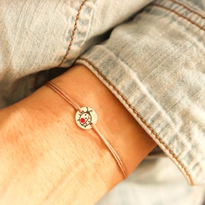 Può includere: Un braccialetto d'argento con un ciondolo a forma di coccinella rossa. Il braccialetto è al polso.